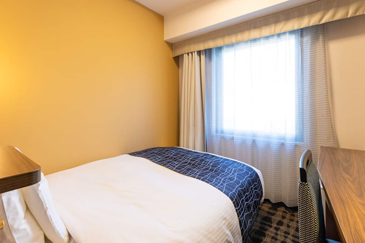 Une chambre d’hôtel avec un lit, un bureau et une fenêtre avec des rideaux.