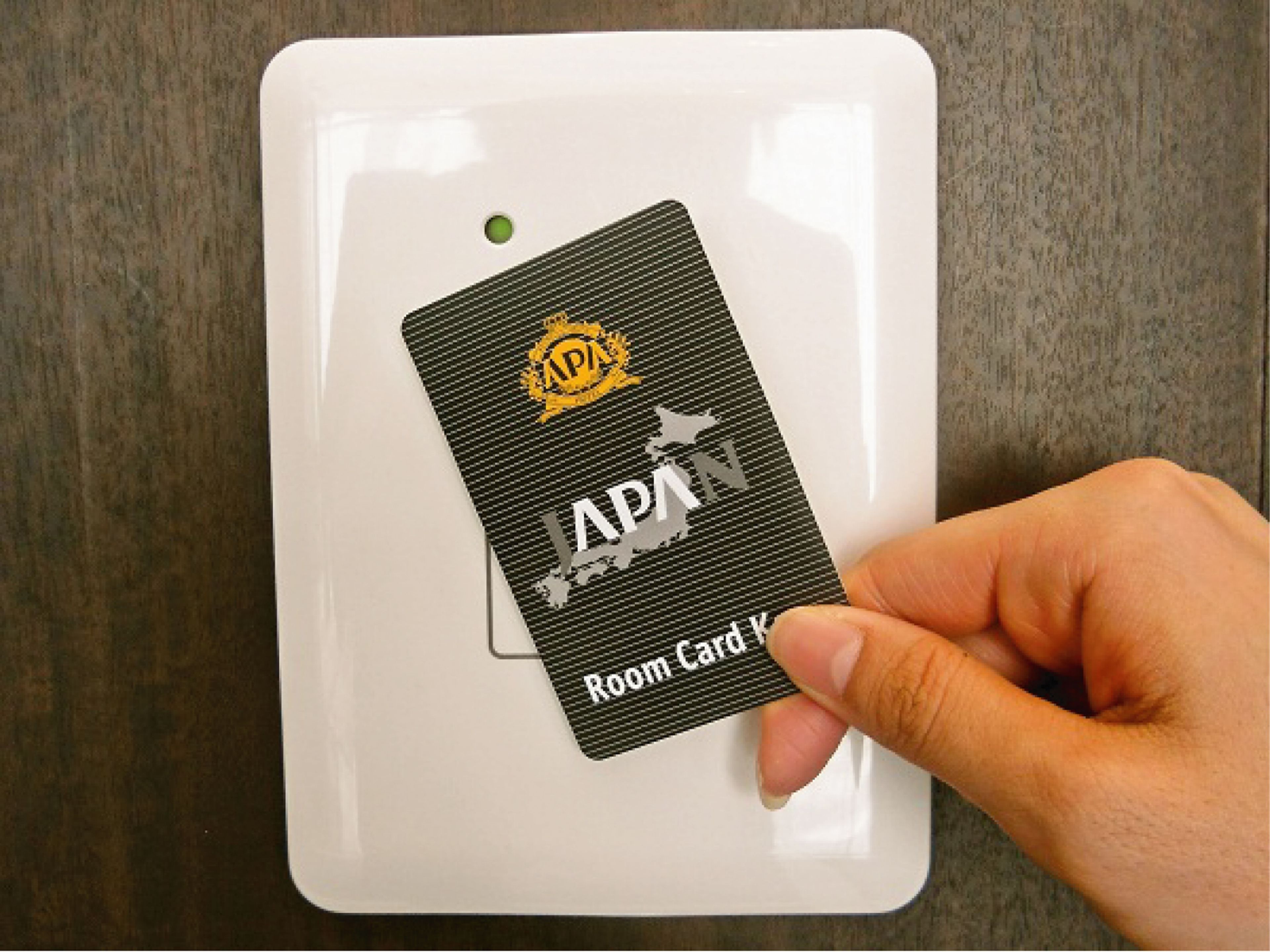 Une main tenant une carte noire sur laquelle figurent les mots « APA » et « Room Card », le tout posé sur une plaque blanche.