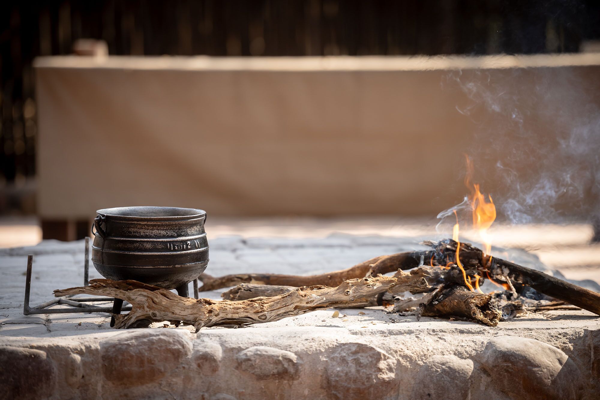 A campfire with logs and a metal pot on a stone surface.
