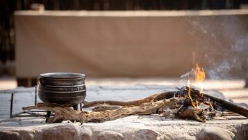 A campfire with logs and a metal pot on a stone surface.