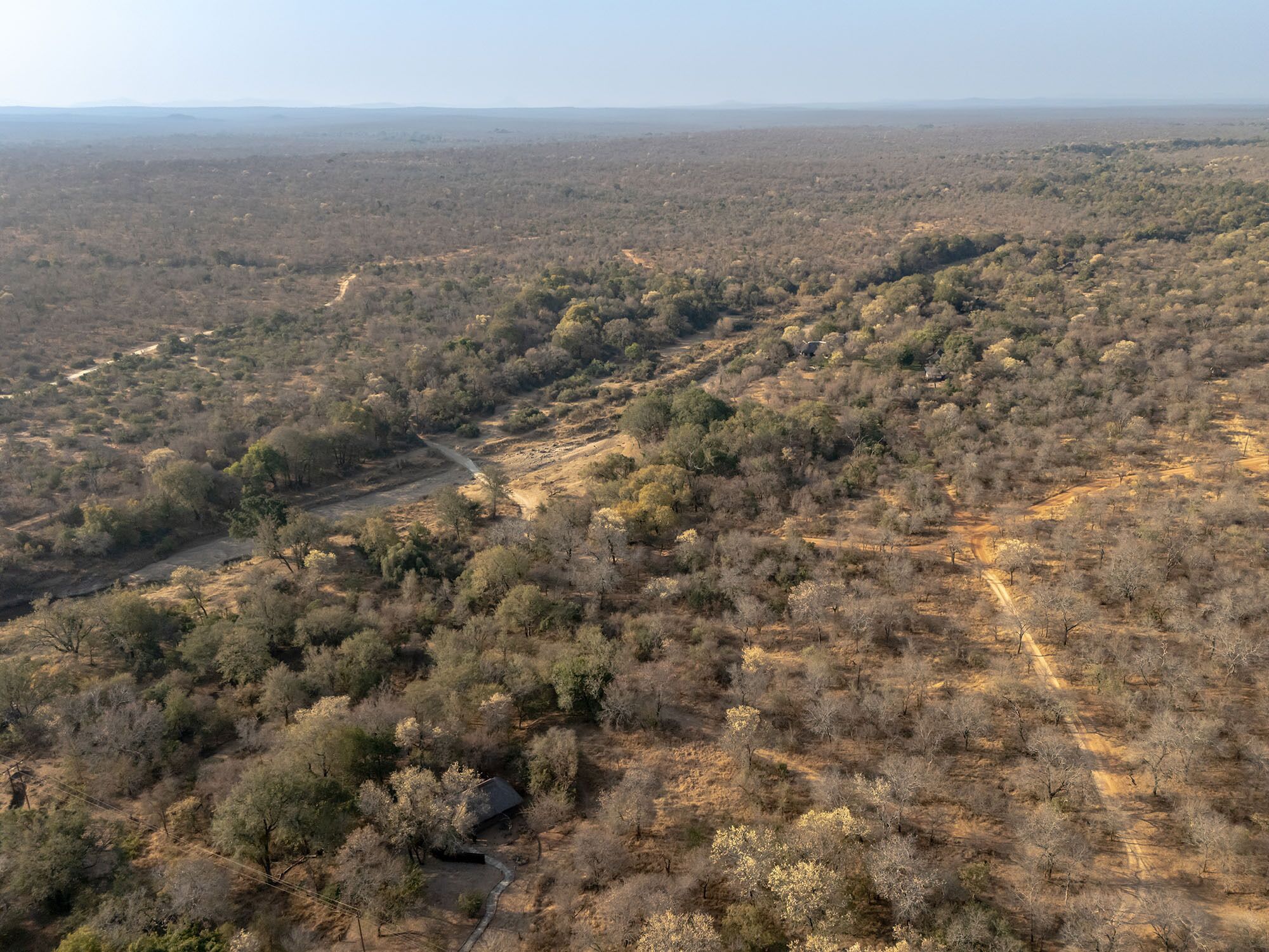 An aerial view of a dry, hilly landscape with sparse vegetation and a few scattered buildings.