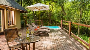 A wooden deck with a pool, lounge chairs, and a table with a bottle of wine and a glass. - Karongwe- Shiduli Safari Lodge (Hoedspruit)