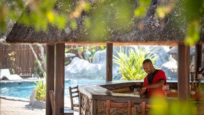 A bar area with a stone counter, wooden chairs, and a pool in the background. - Karongwe- Shiduli Safari Lodge (Hoedspruit)