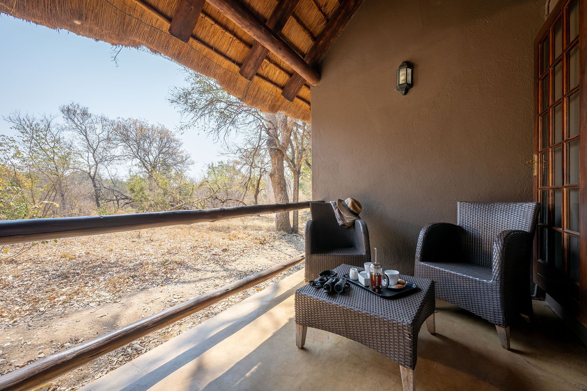 A balcony with wicker furniture, a table with binoculars and a tray, and a view of a dry landscape with trees.