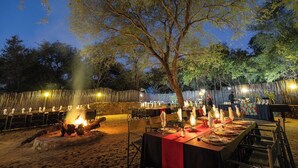 An outdoor dining area with tables set for a meal, a fire pit, and a bamboo fence. - Karongwe- Shiduli Safari Lodge (Hoedspruit)