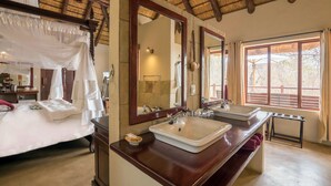 A bedroom with a canopy bed, a large mirror, a vanity with a sink, and a window with a view of trees. - Karongwe- Shiduli Safari Lodge (Hoedspruit)