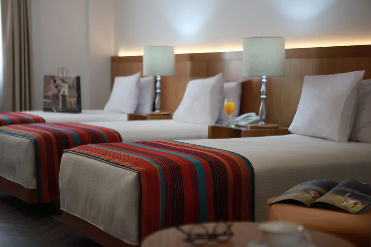 A hotel room with two beds, a nightstand with a lamp, a bedside table with a glass of orange juice, and a magazine on the table.