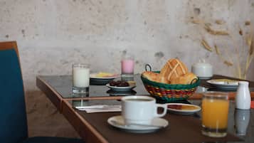 Una mesa de desayuno con una cesta de pan, un vaso de leche, una taza de café, un plato de huevos y un vaso de zumo de naranja.