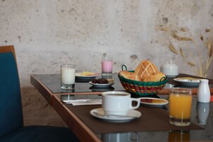 Una mesa de desayuno con una cesta de pan, un vaso de leche, una taza de café, un plato de huevos y un vaso de zumo de naranja.