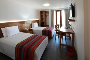 A hotel room with two beds, a desk, a chair, a TV, and a wardrobe.