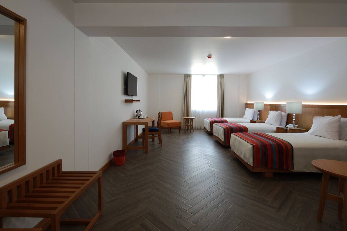 A hotel room with two beds, a desk, a chair, a TV, and a large mirror.