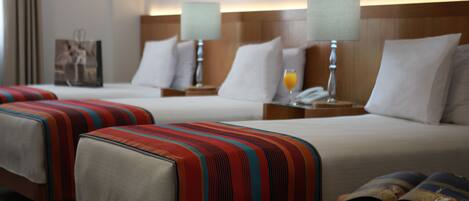 A hotel room with two beds, each with a striped bedspread, bedside lamps, and a nightstand with a phone and a glass of orange juice.