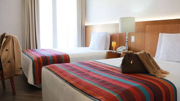 Una habitación de hotel con dos camas, una mesita de noche, una lámpara y un perchero.