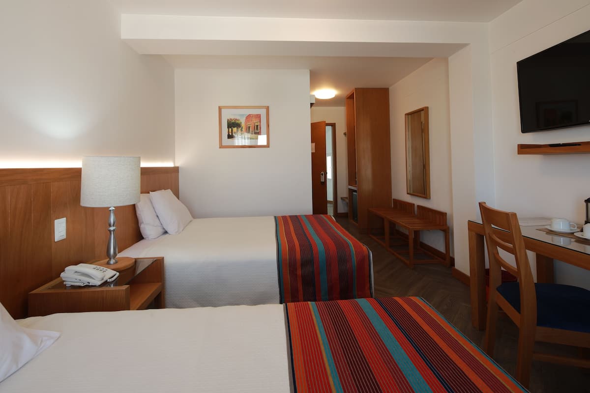 A hotel room with two beds, a desk, a chair, a TV, and a framed picture on the wall.
