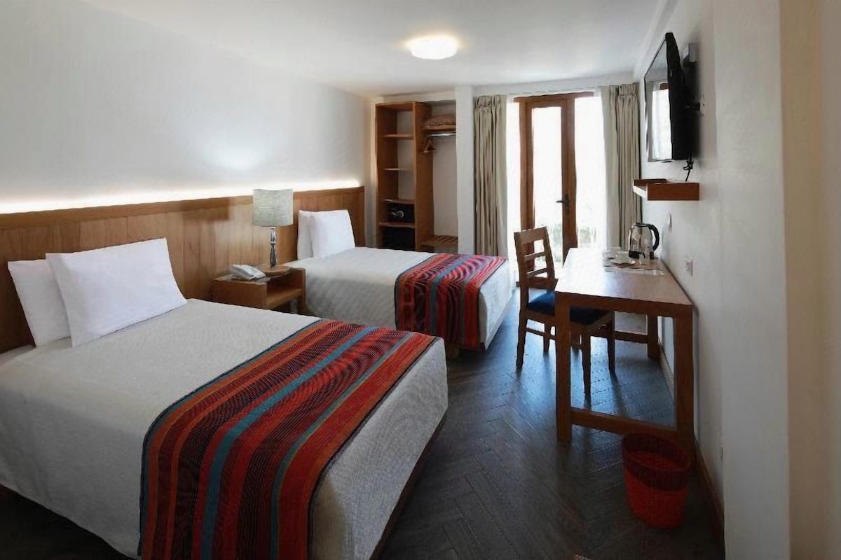 Habitación de hotel con dos camas, un escritorio, una silla, un televisor y un armario.
