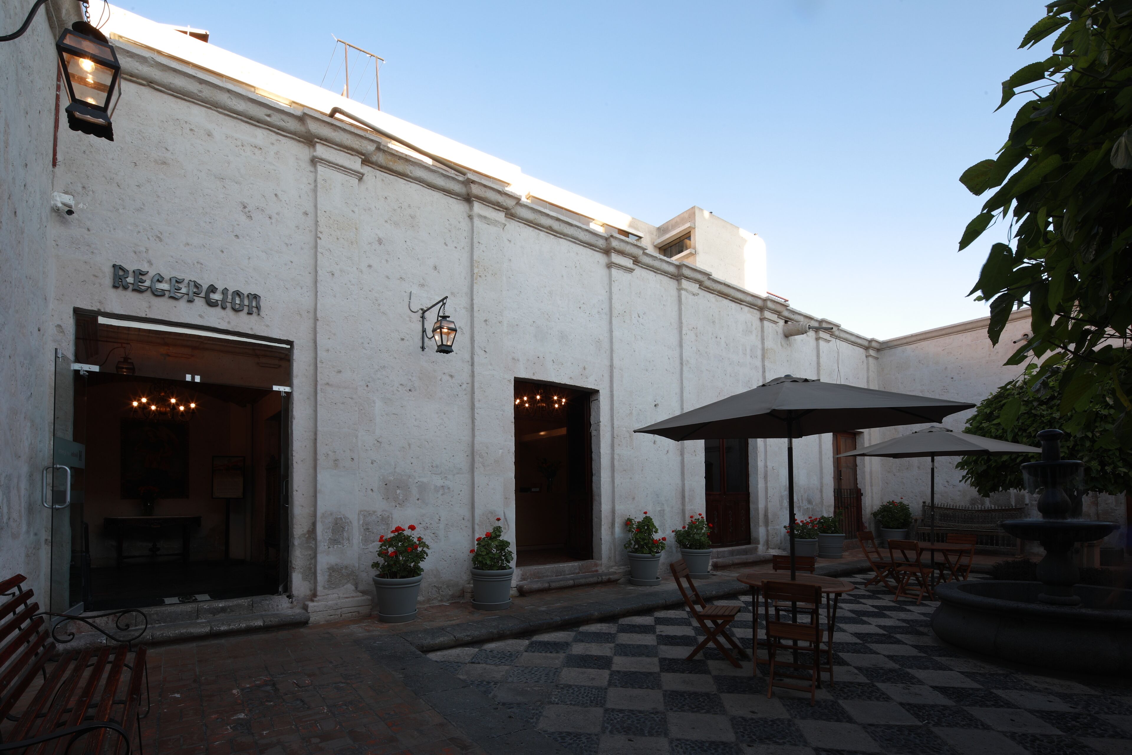 A building with a reception area, outdoor seating with umbrellas, and potted plants.