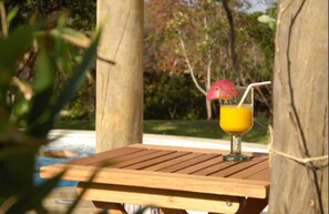 Una mesa de madera con un vaso de jugo de naranja y una pajita, atada a un árbol.