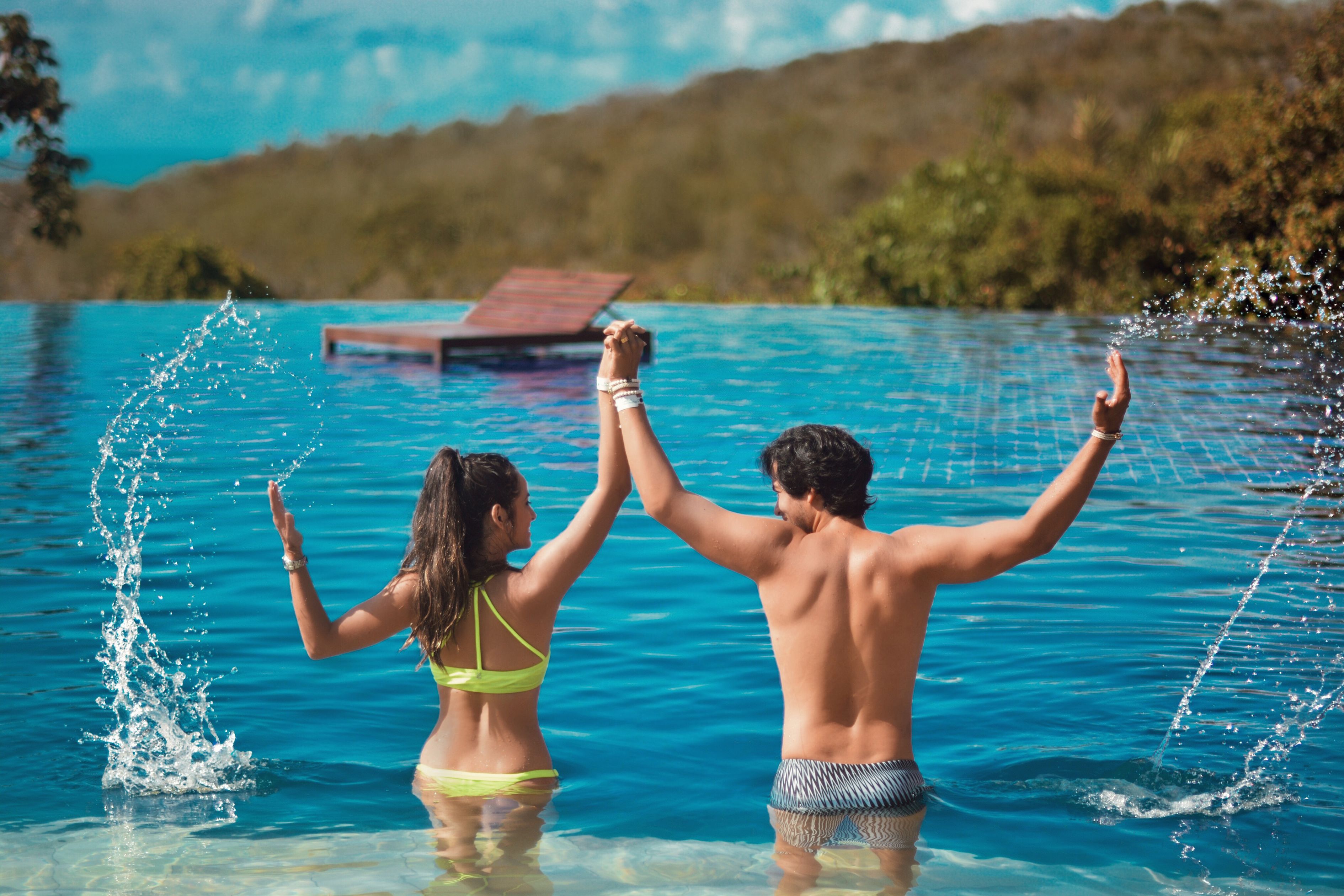 Una pareja en una piscina con agua azul cristalina, rodeada de follaje.