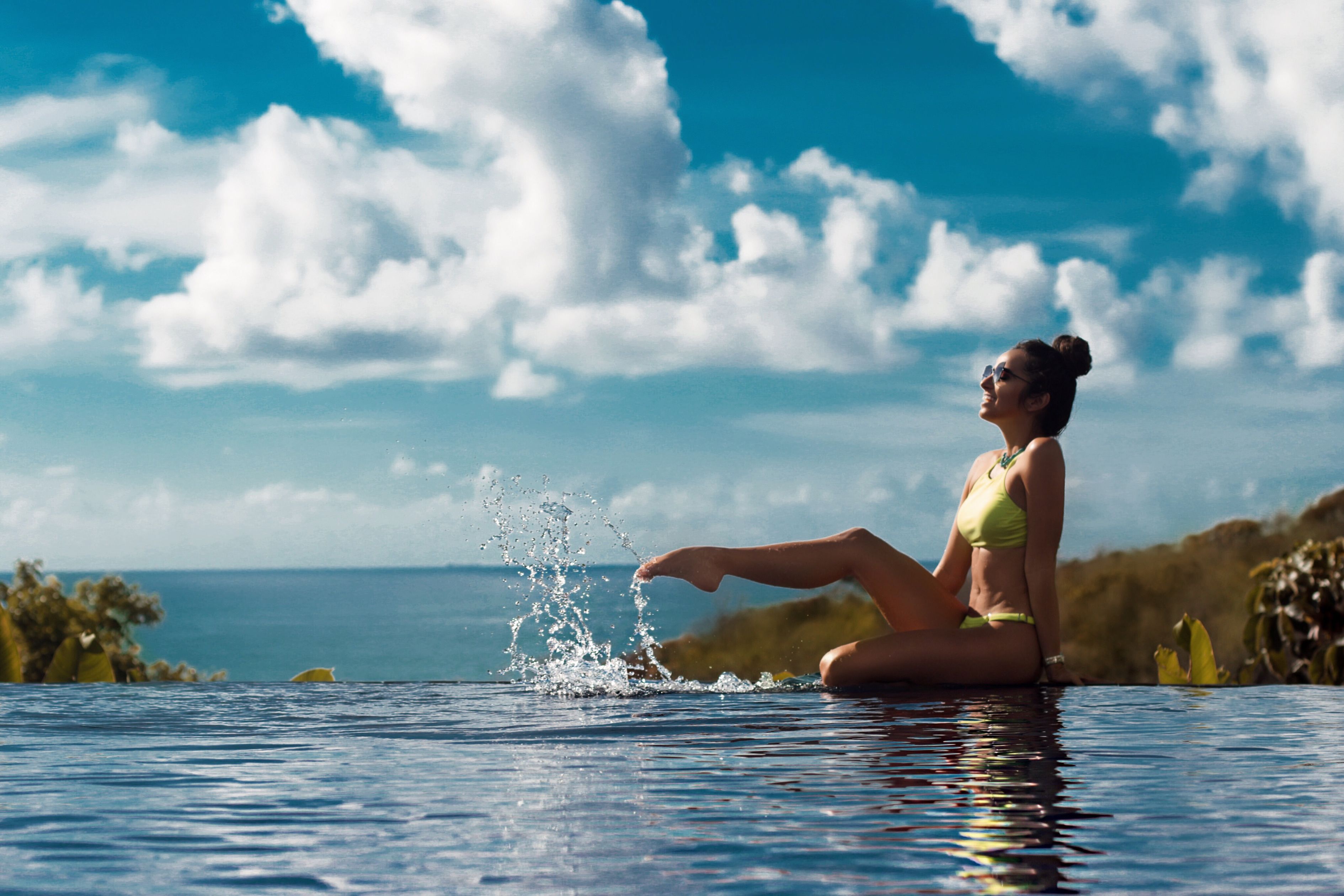 A person sitting by a pool with a clear view of the ocean and sky.