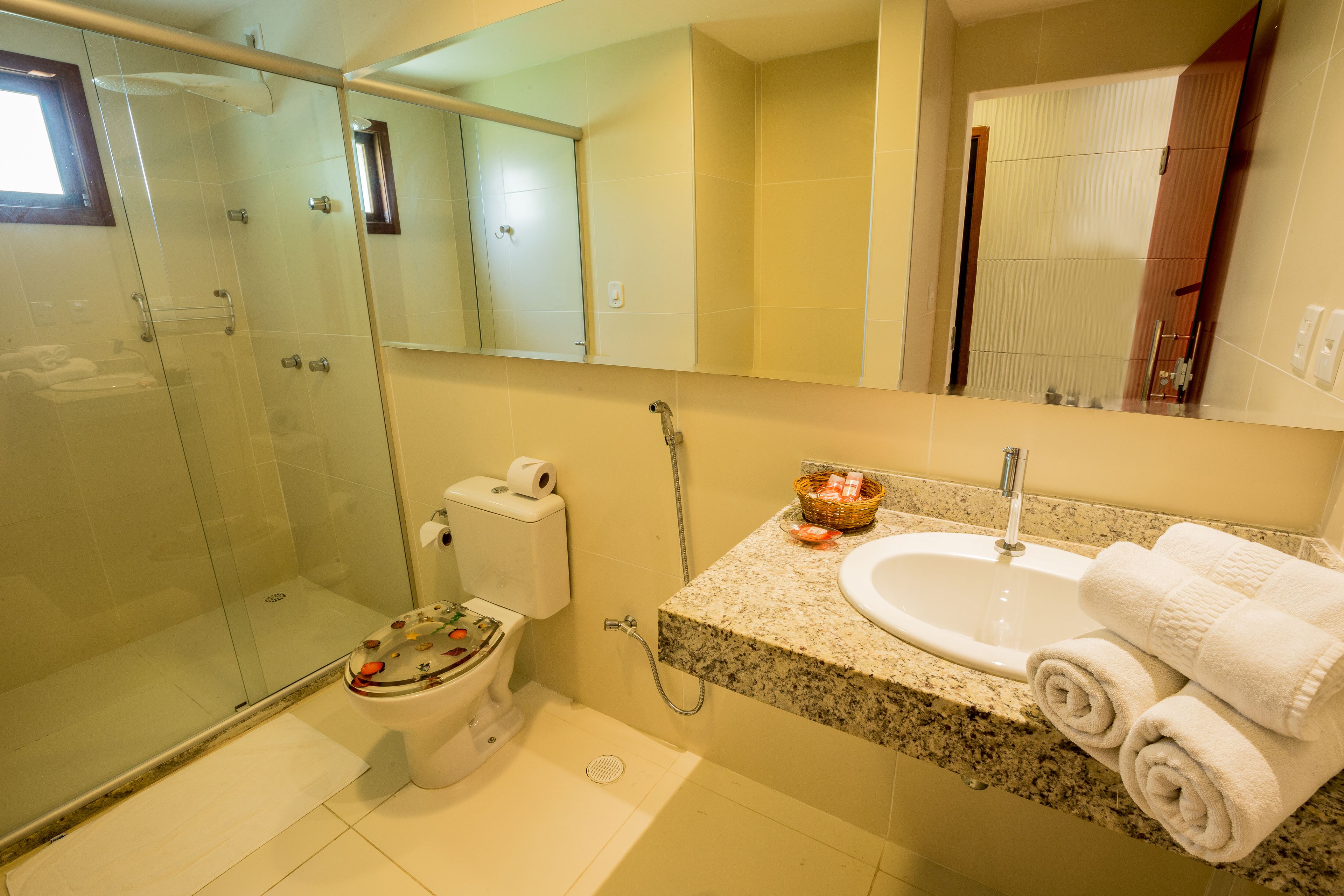 Baño con cabina de ducha de vidrio, inodoro, lavamanos con encimera de granito y espejo sobre el lavamanos.