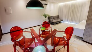 Una sala de estar moderna con una mesa de comedor de vidrio, sillas rojas, un sofá y una lámpara colgante grande.