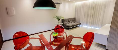 Un salon moderne avec une table à manger en verre, des chaises rouges, un canapé et un grand luminaire suspendu.