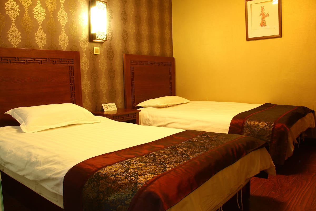 Two single beds with wooden headboards, a nightstand with a telephone, and a framed picture on the wall.