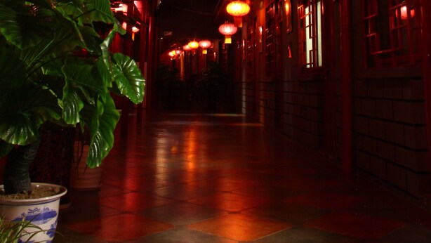 A corridor with red lanterns hanging from the ceiling and potted plants along the walls. - The Classic Courtyard (Beijing)