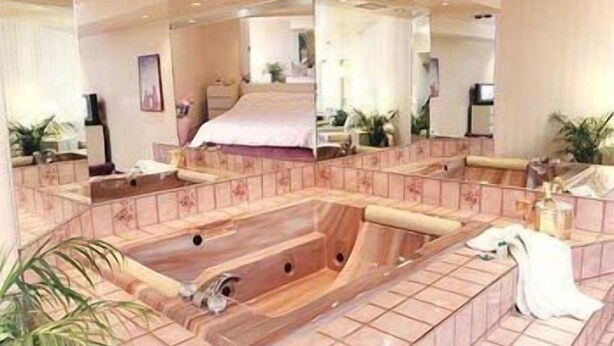 Un baño tipo spa con una bañera grande de madera, un espejo y una cama al fondo.
