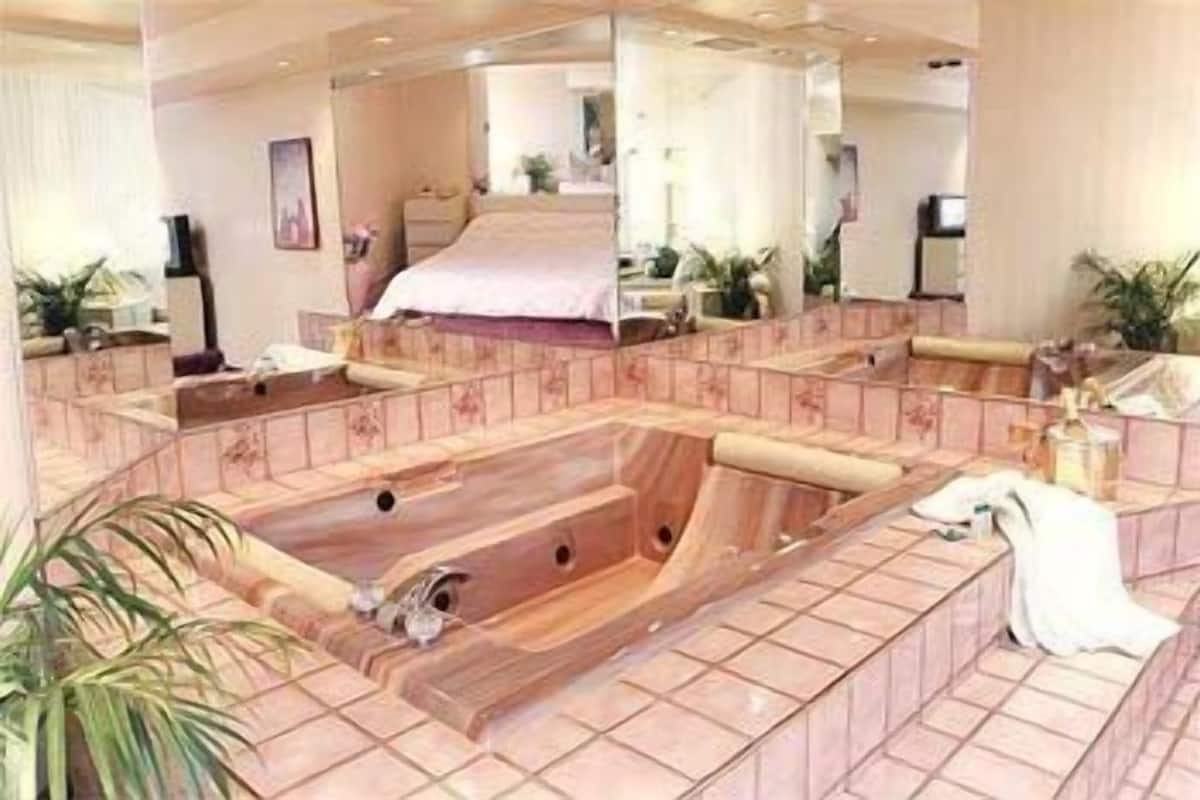 Un baño tipo spa con una bañera grande de madera, un espejo y una cama al fondo.