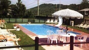 Una piscina con área techada, sillas de descanso y zona de césped.