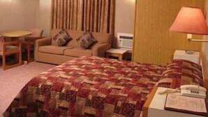 Una habitación de hotel con cama, sofá, mesita, lámpara y microondas.