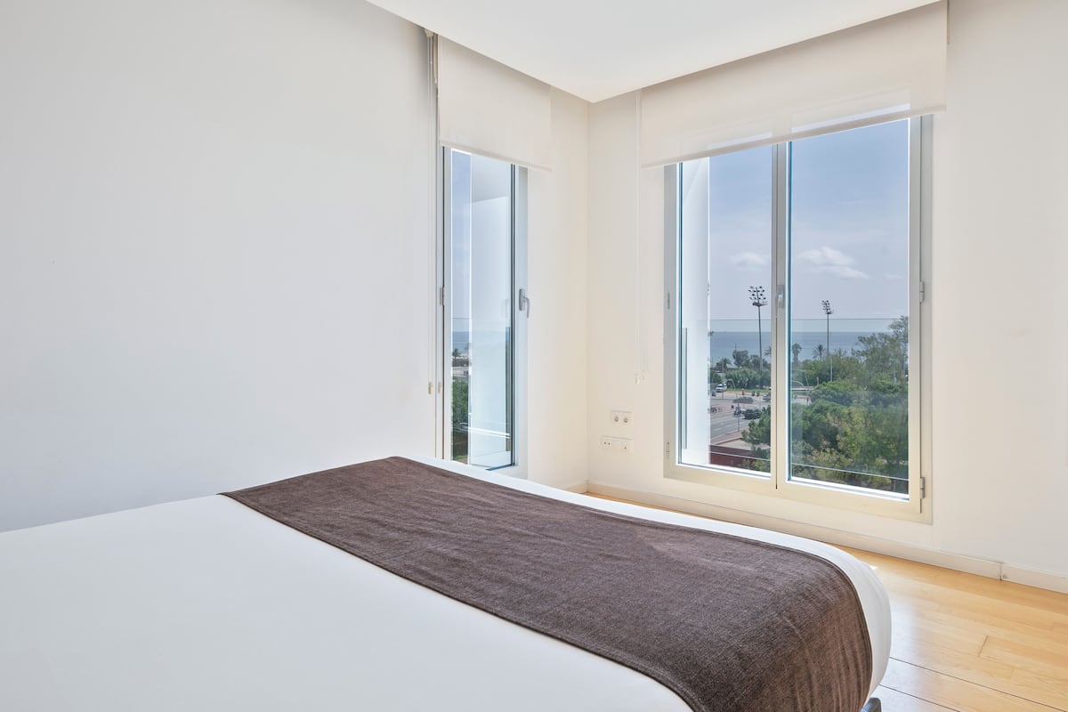 A modern bedroom with a large bed, a view of the city through floor-to-ceiling windows, and a minimalist design.