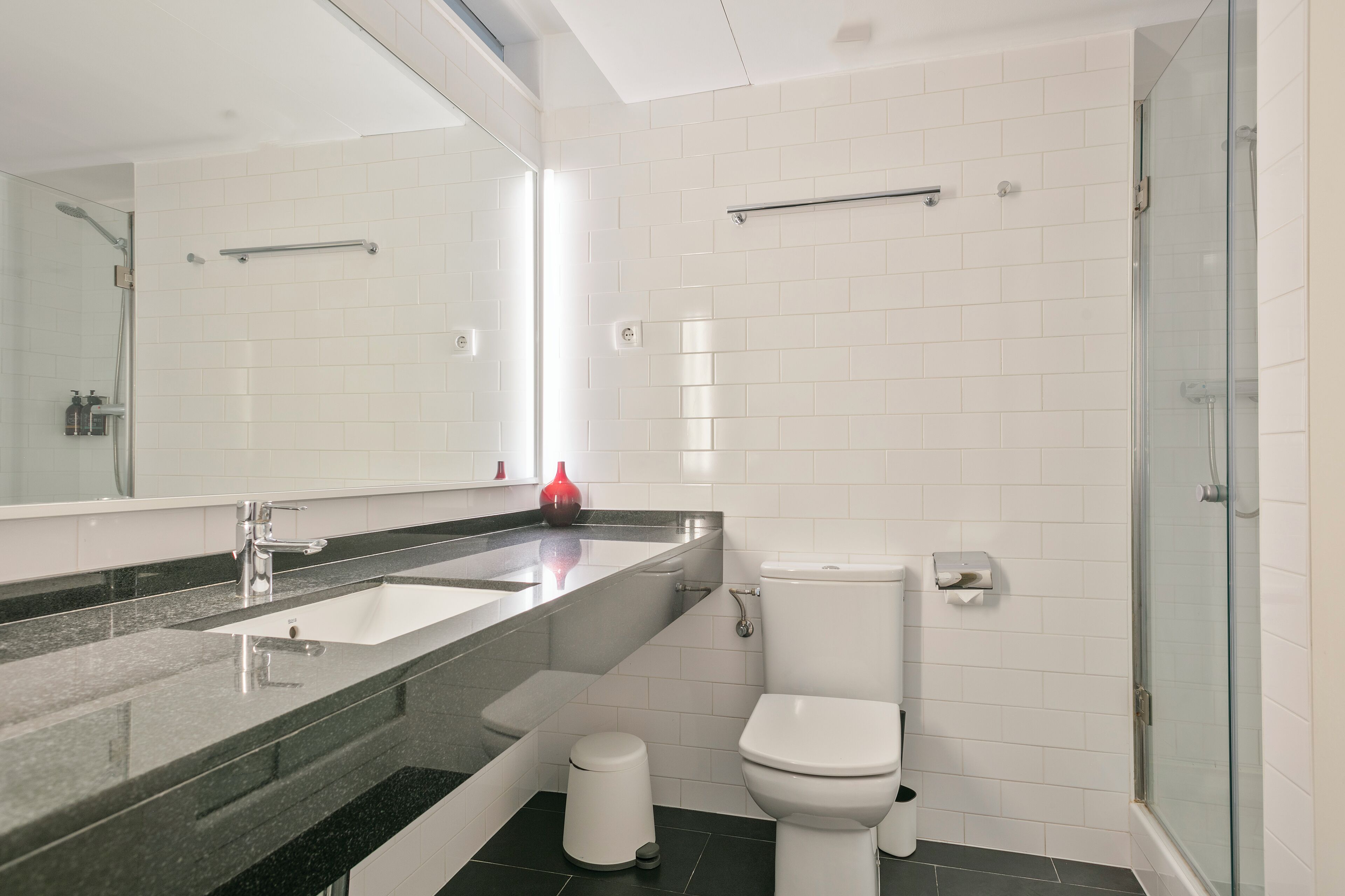A modern bathroom with a large mirror, a sink, a toilet, and a glass shower enclosure.