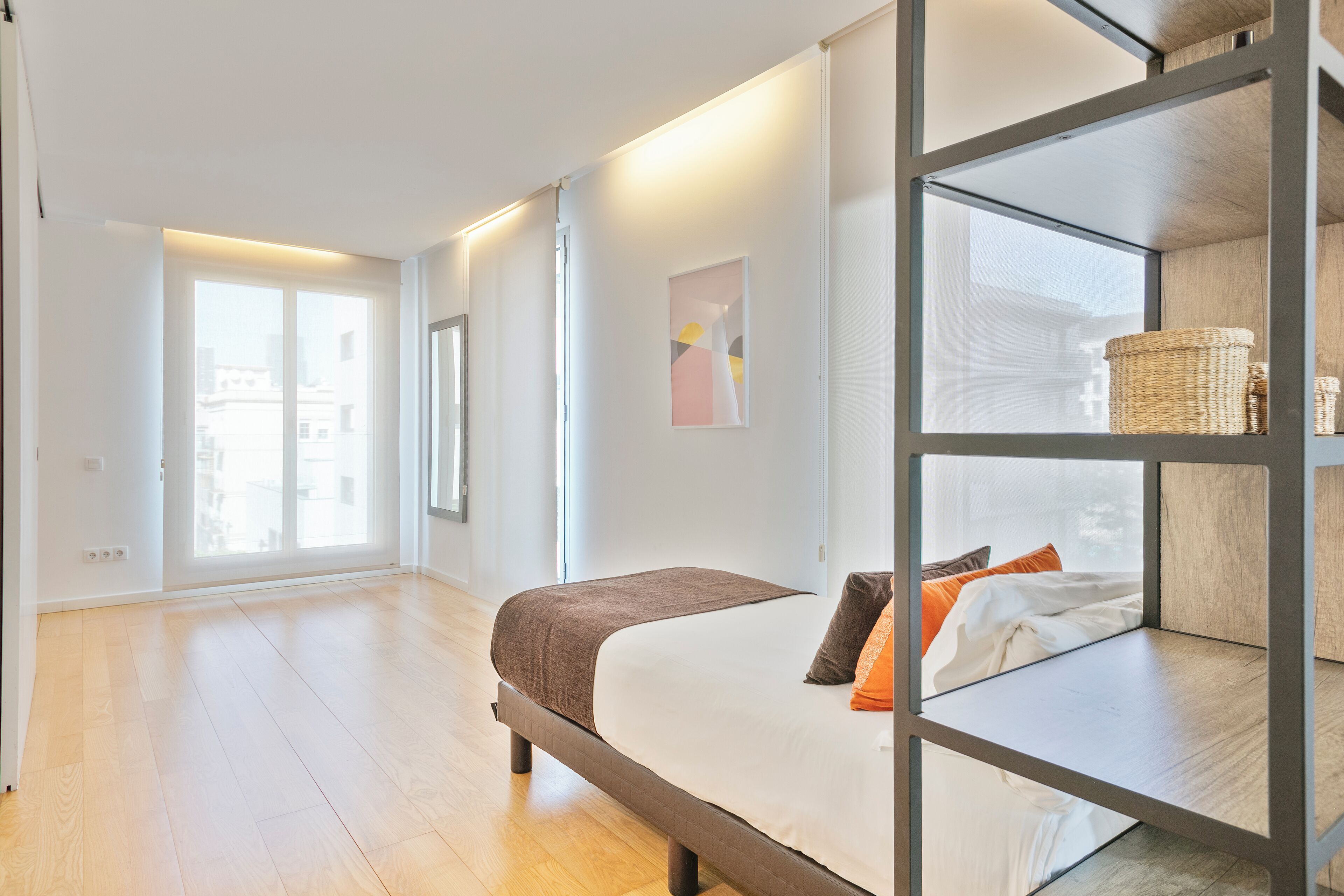 A modern bedroom with a large bed, a wooden floor, and a view of the city through large windows.