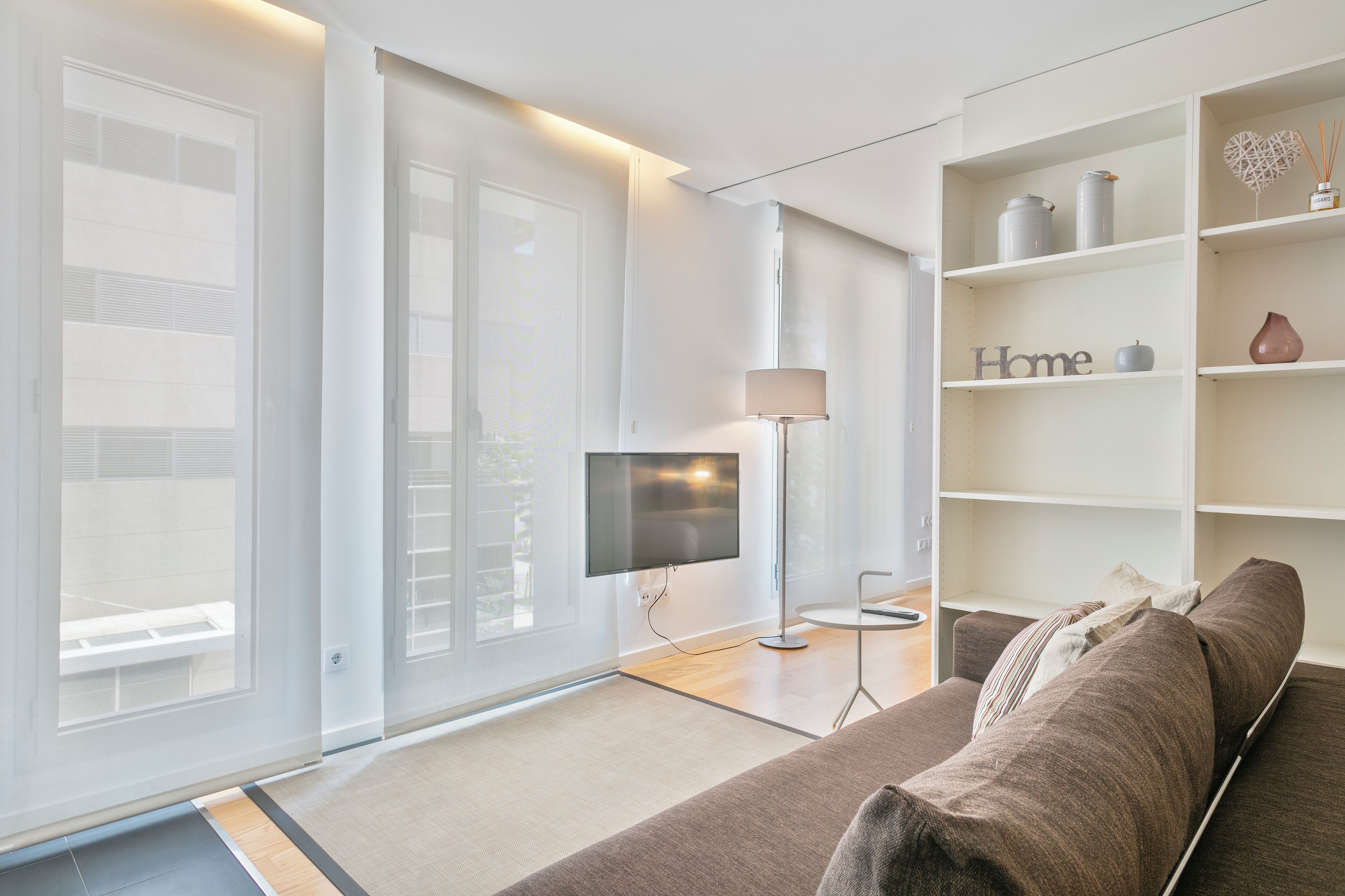 A modern living room with a sofa, a television, a lamp, and a bookshelf.