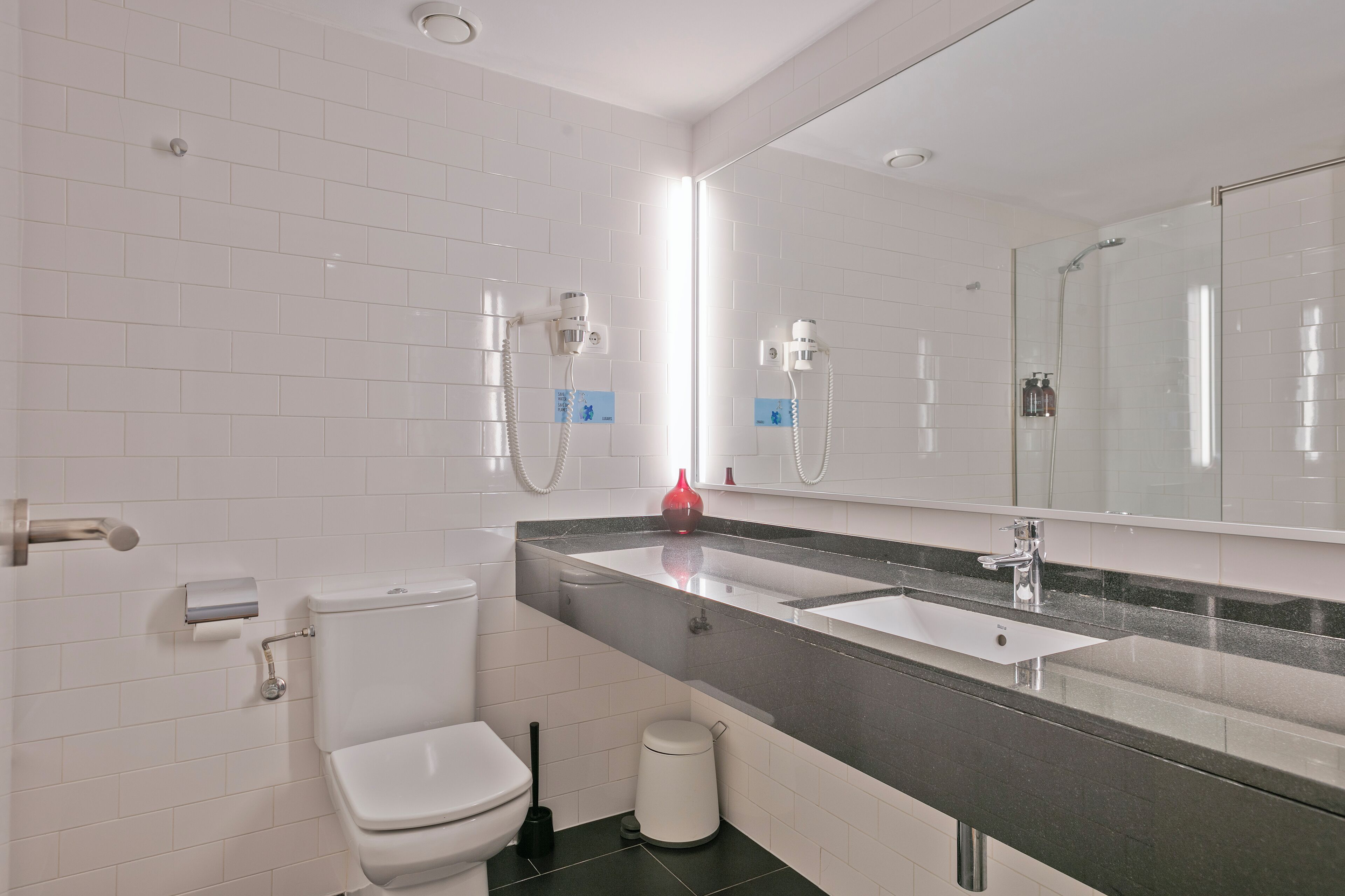 A modern bathroom with white tiled walls, a black countertop, a white sink, and a toilet.