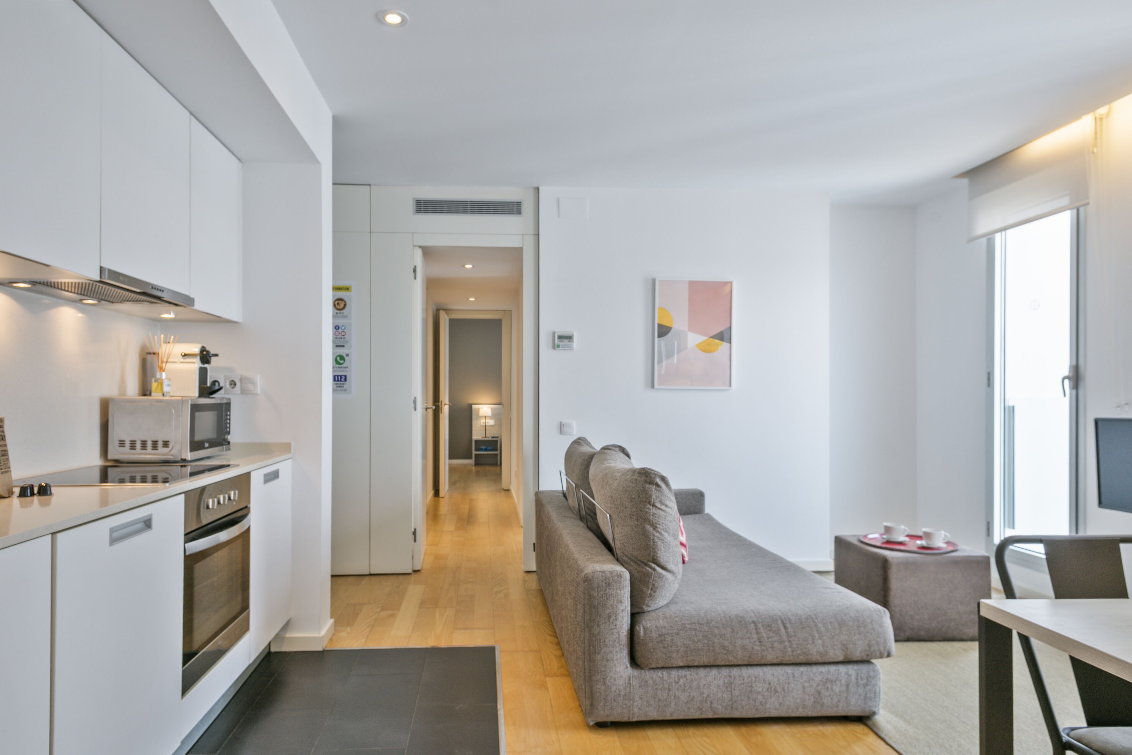 A modern kitchen with built-in appliances, a grey sofa, and a dining area with a table and chairs.