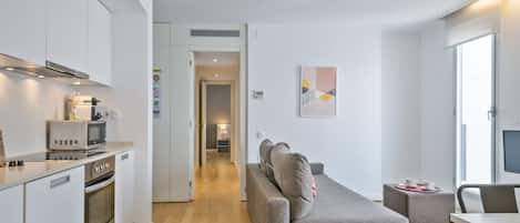 A modern kitchen with built-in appliances, a grey sofa, and a dining area with a table and chairs.