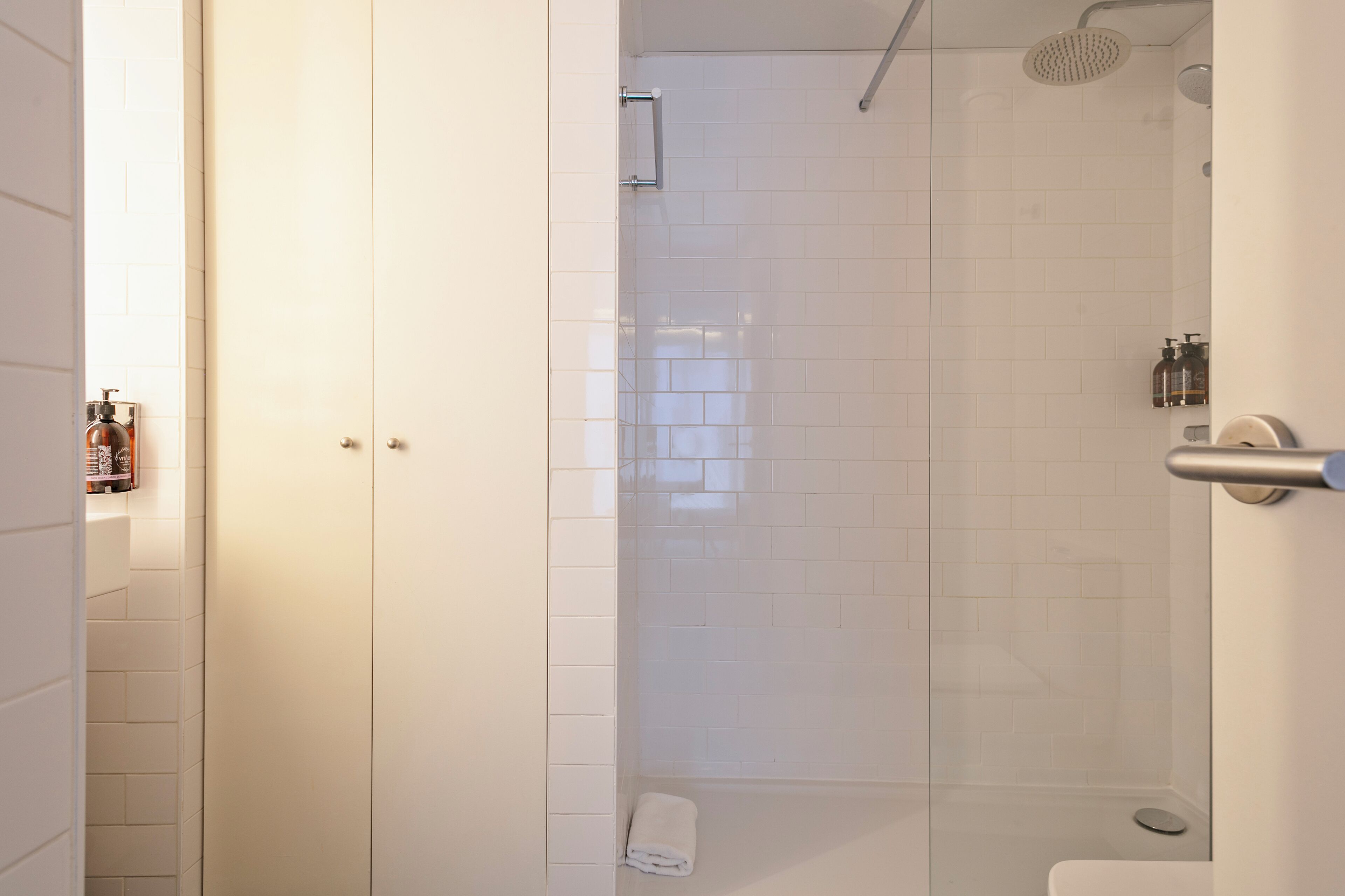 A modern bathroom with white tiles, a glass shower enclosure, a toilet, and a towel rack.
