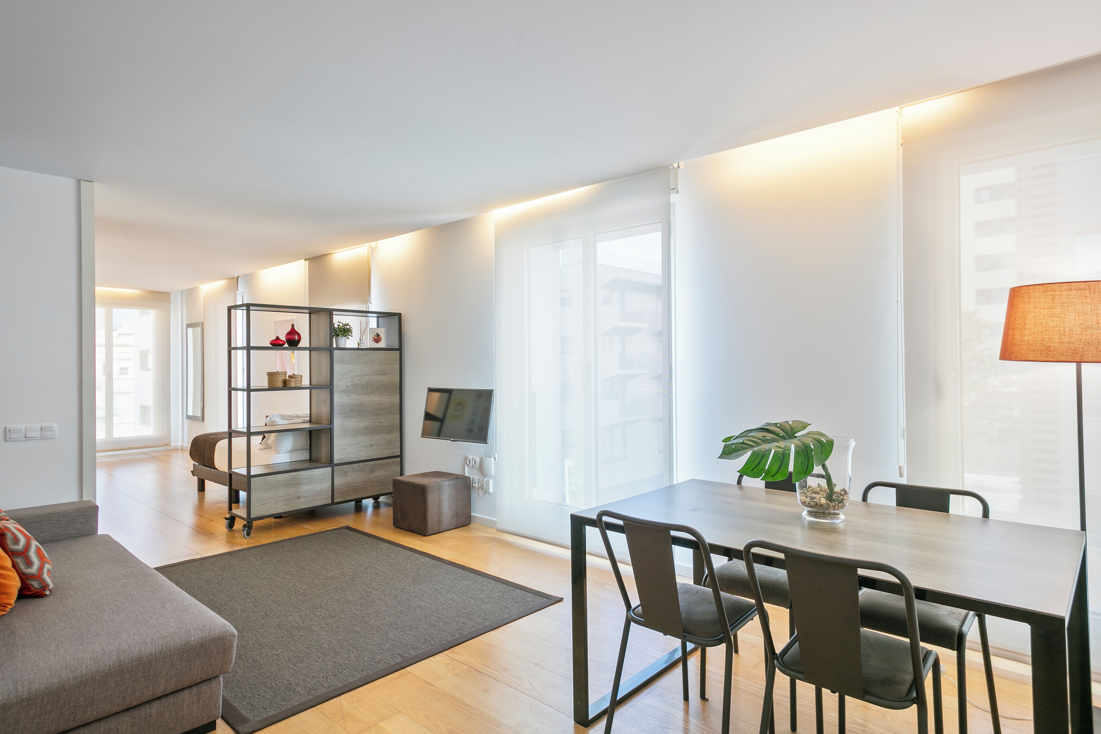 A modern living room with a sofa, a dining table with chairs, a TV, and a bookshelf.