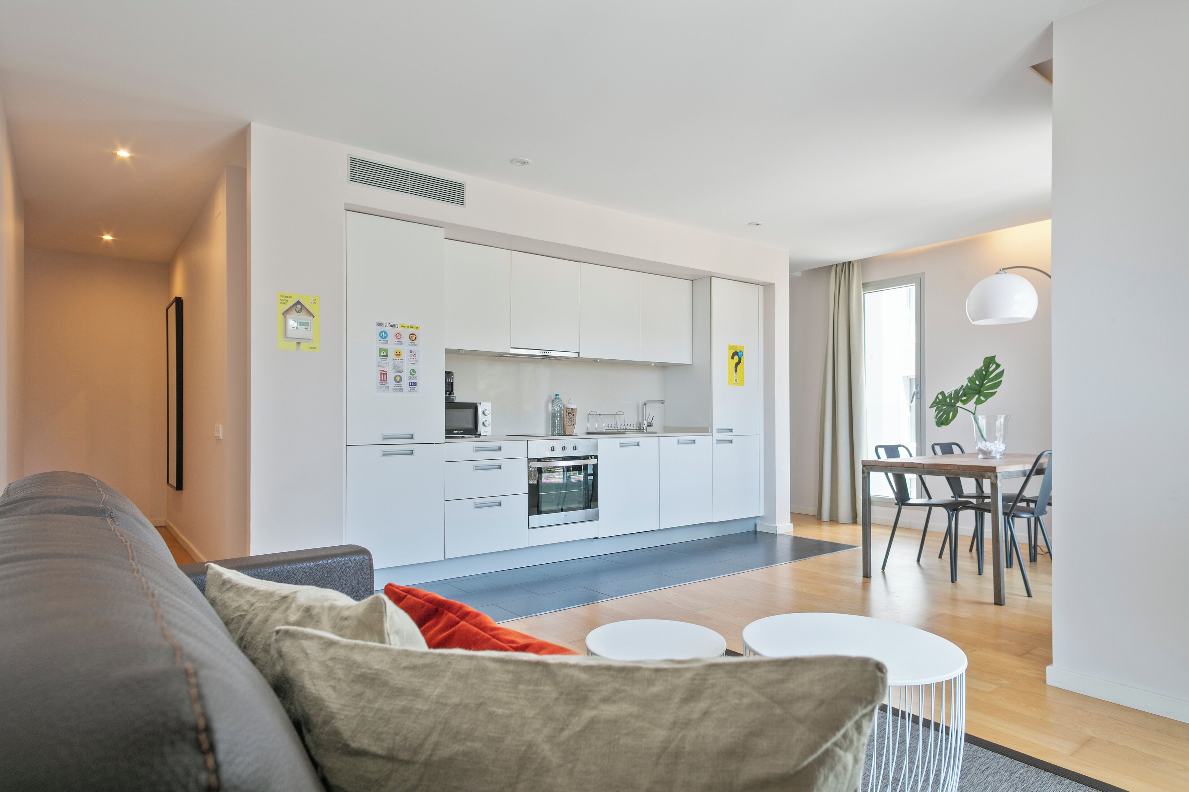 A modern living room with a grey sofa, a small round table, and a dining area with a table and chairs.