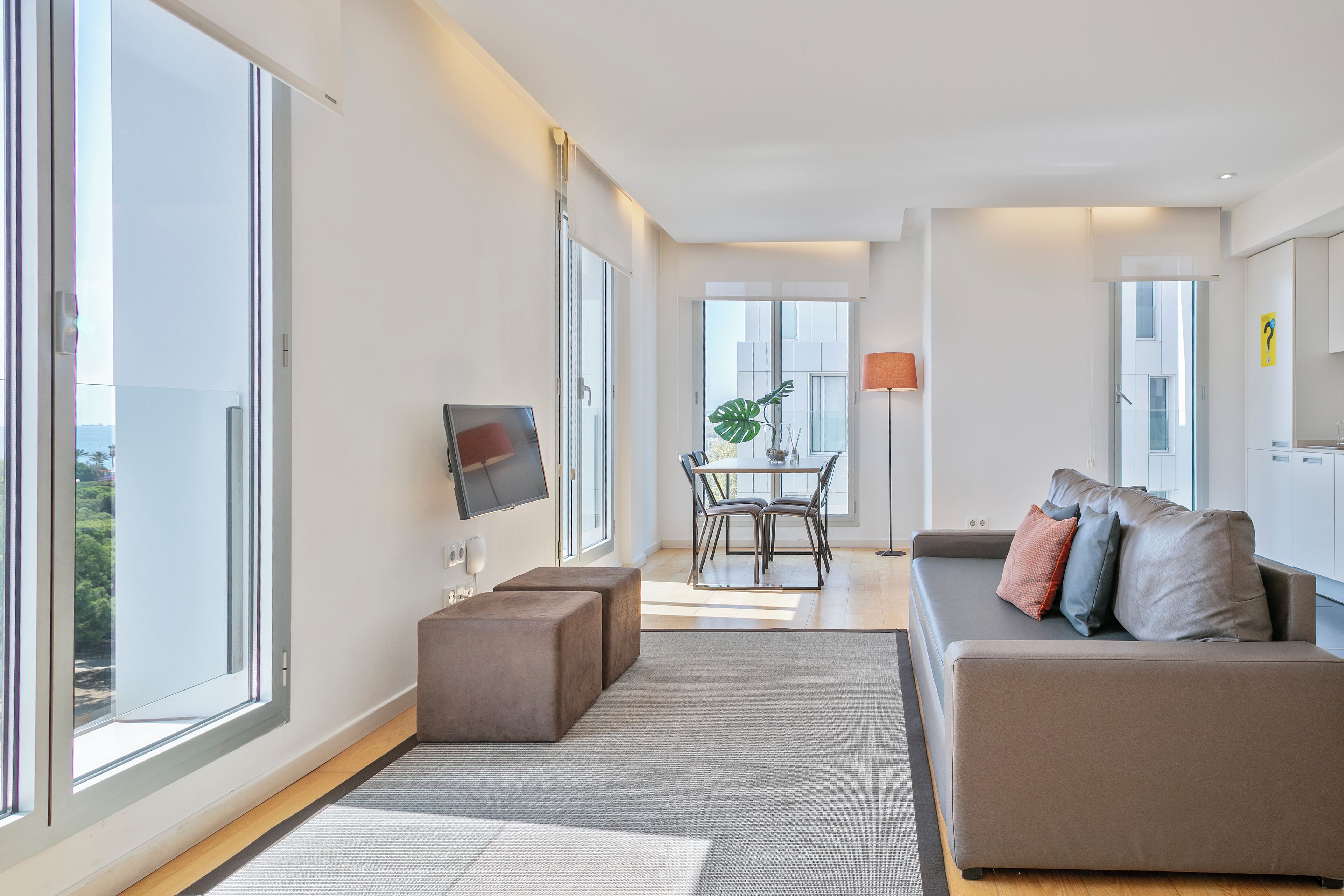 A modern living room with a sofa, ottomans, a TV, and a dining area with a table and chairs.