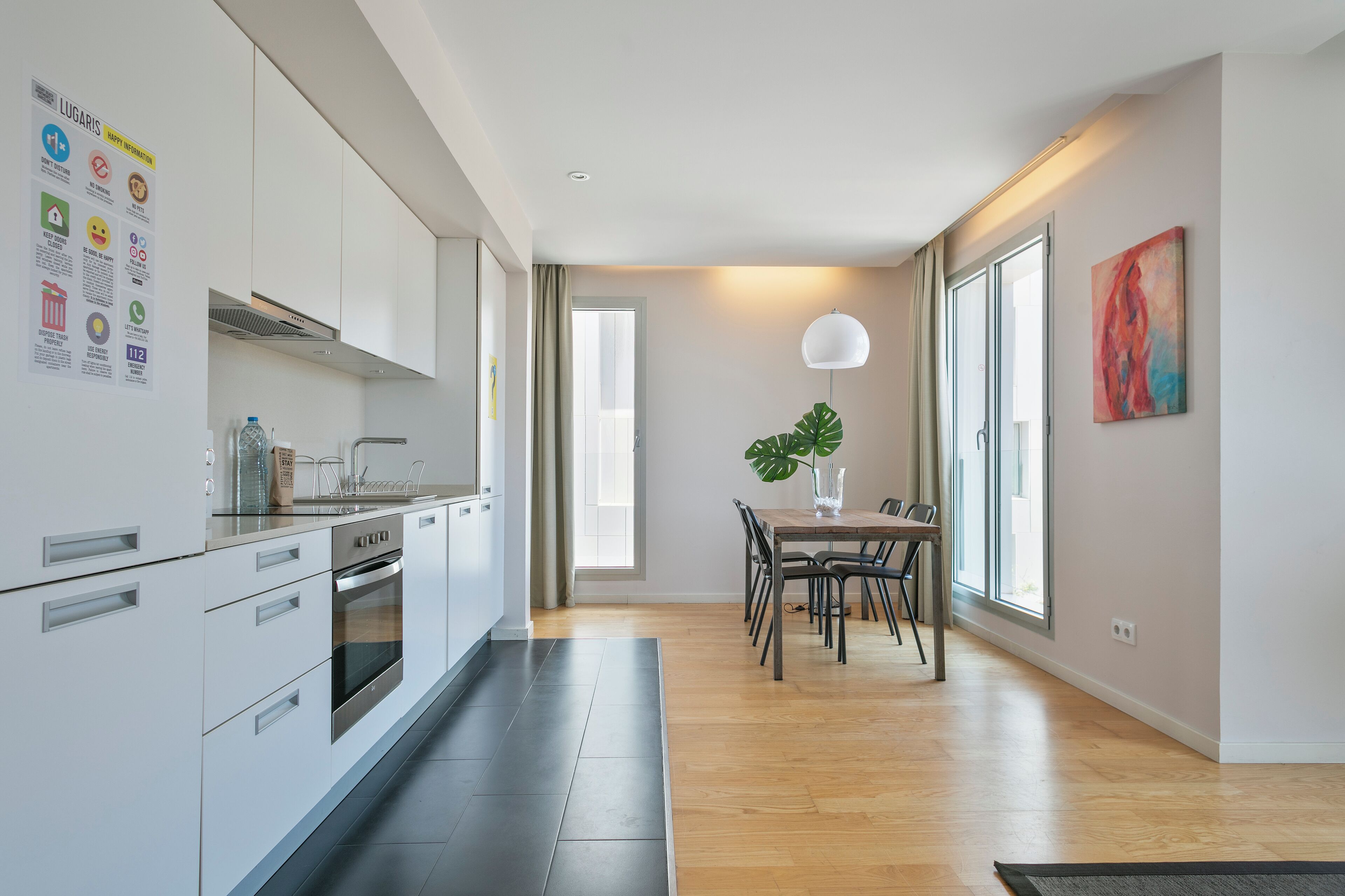 A modern kitchen with white cabinets, a built-in oven, and a dining area with a wooden table and chairs.