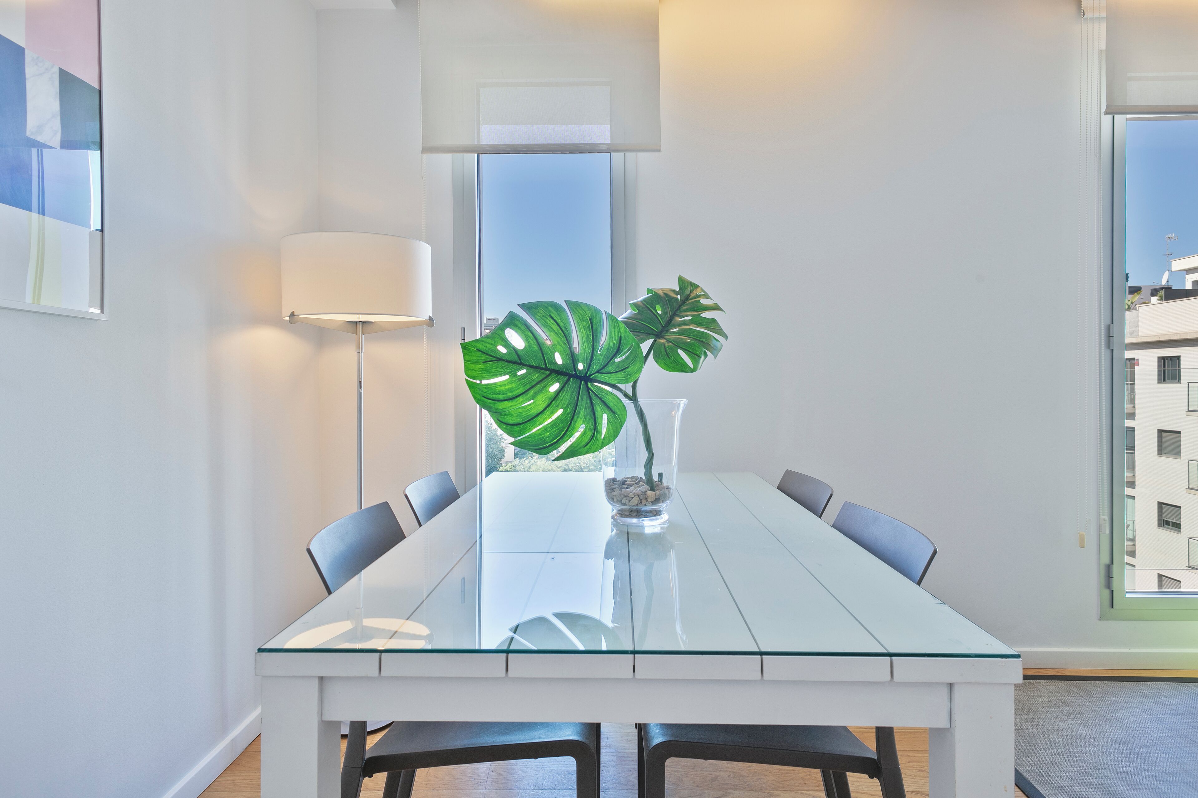 A modern dining room with a glass table, chairs, a potted plant, and a lamp.
