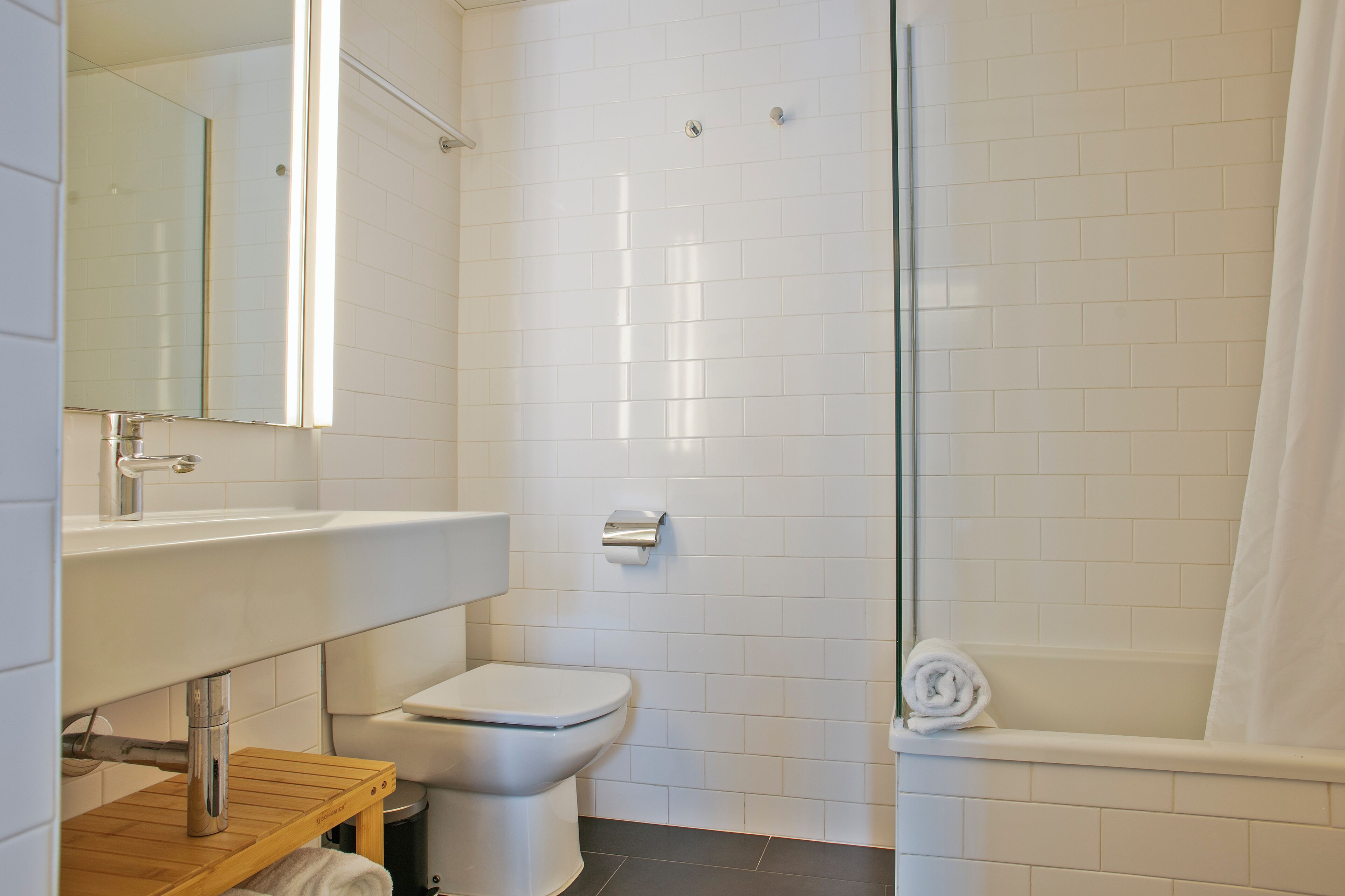 Une salle de bain moderne avec un lavabo, des toilettes et une zone de douche, le tout de couleur blanche.