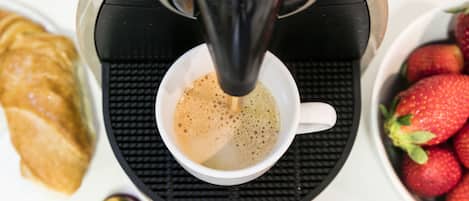 Una máquina de café sirviendo café en una taza, un croissant y un cuenco con fresas.