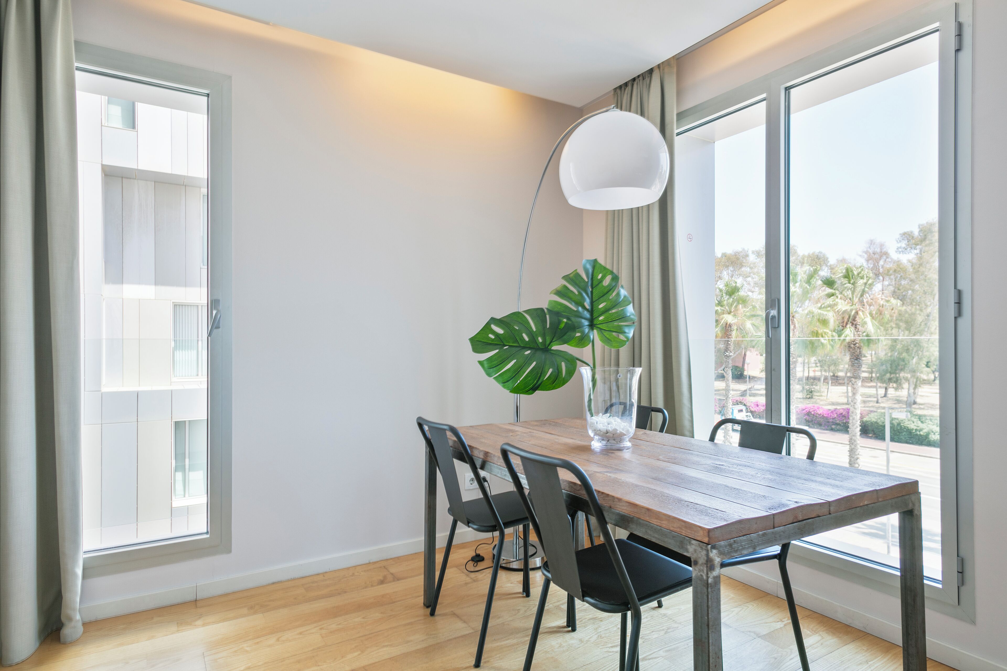 Un comedor con una mesa de madera, cuatro sillas, una planta en maceta y una lámpara de pie.