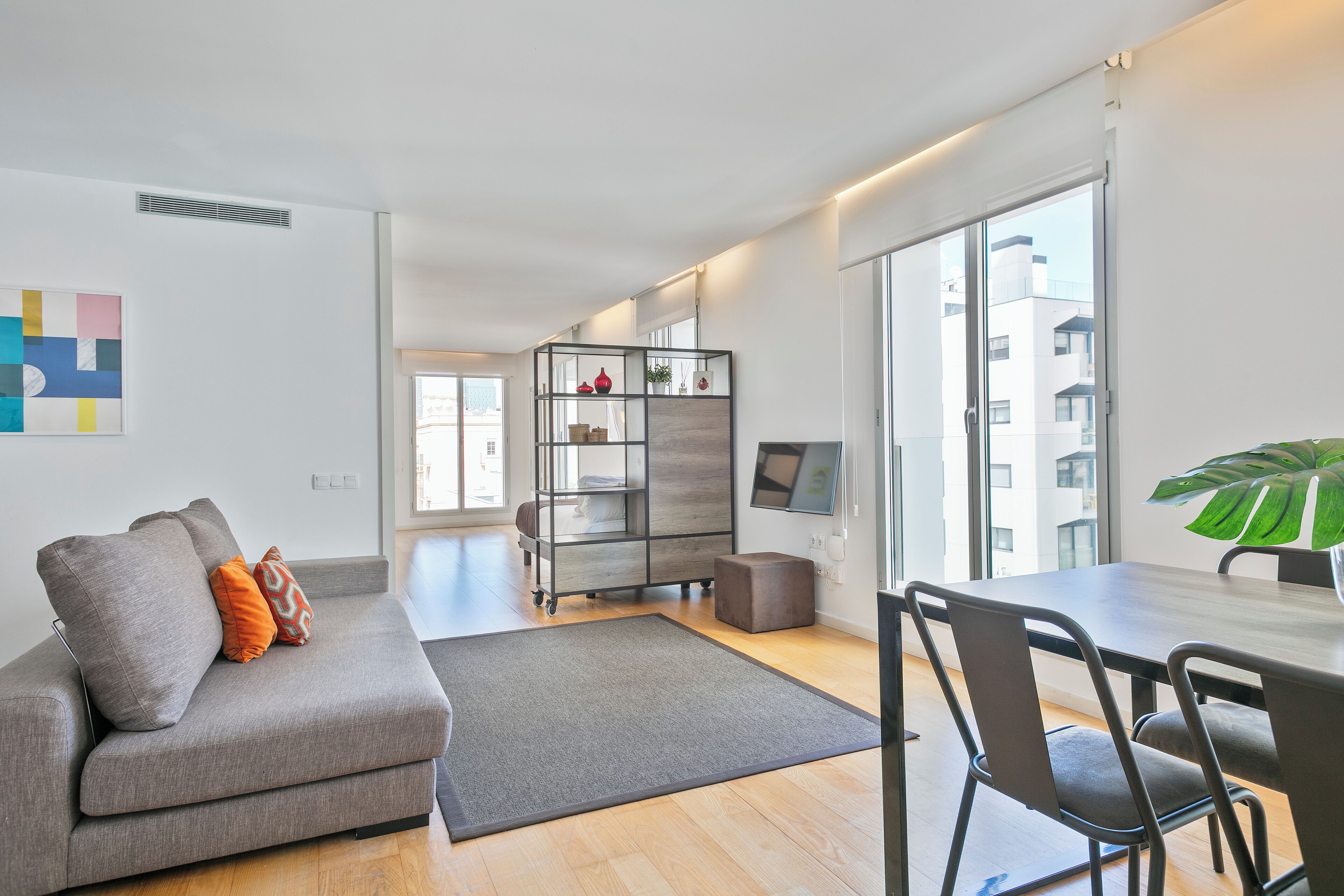 En moderne stue med en grå sofa, et spisebord og et stort vindue.
