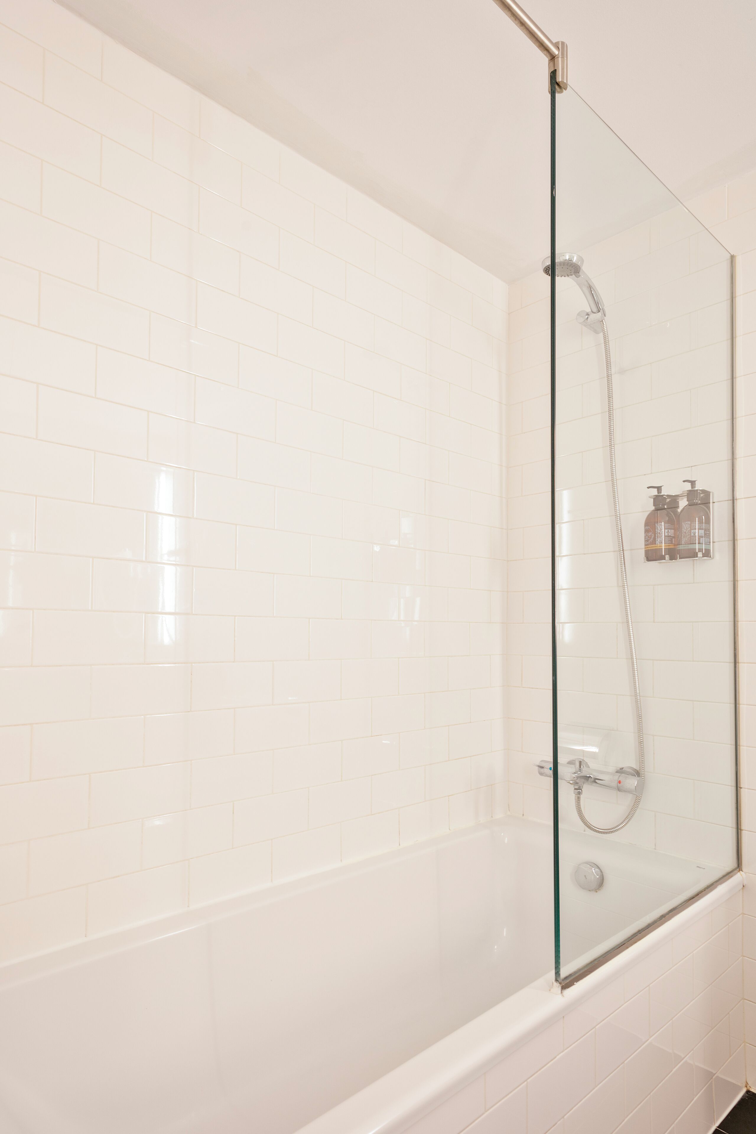 A glass-enclosed shower area with white tiles and a handheld showerhead.